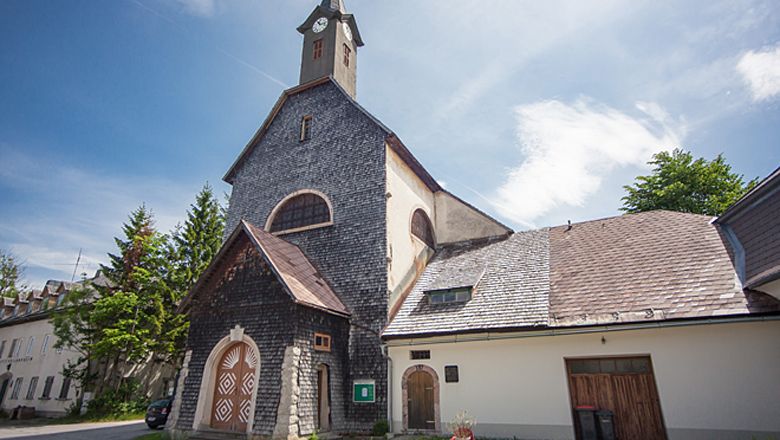 Pfarrkirche Josefsberg mit steinverkleideter Fassade und Turm unter blauem Himmel.