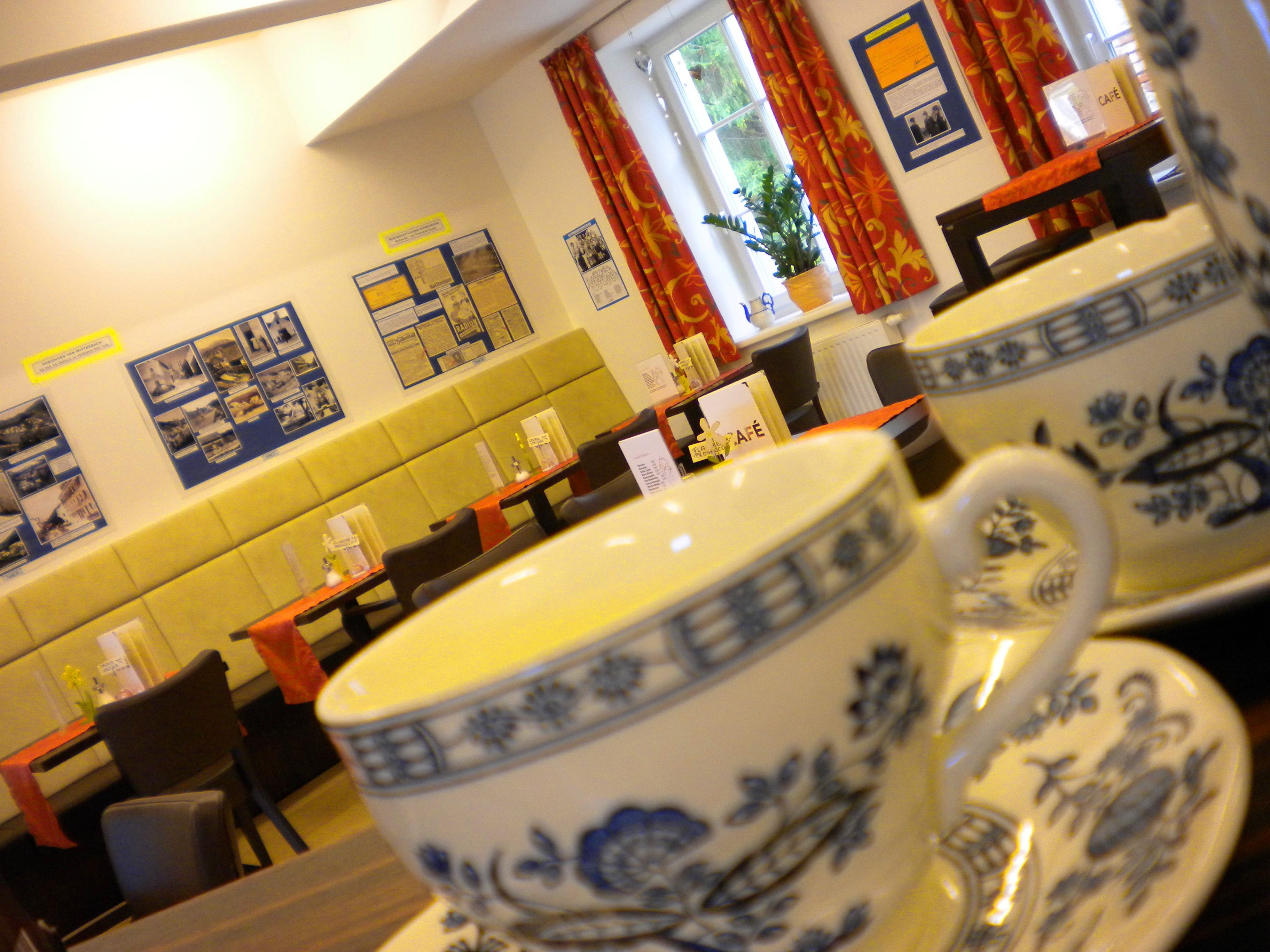 Innenansicht eines Cafés mit Teetassen im Vordergrund und dekorierten Wänden im Hintergrund.