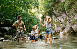 Eine fröhliche Familie genießt einen unbeschwerten Tag im klaren Wasser eines plätschernden Baches. Umgeben von üppigem Grün und majestätischen Felsen, spritzen die Kinder lachend Wasser, während die Erwachsenen die erfrischende Natur erleben. Hier im Naturpark Ötscher Tormäuer wird der Sommer in seiner schönsten Form zelebriert.