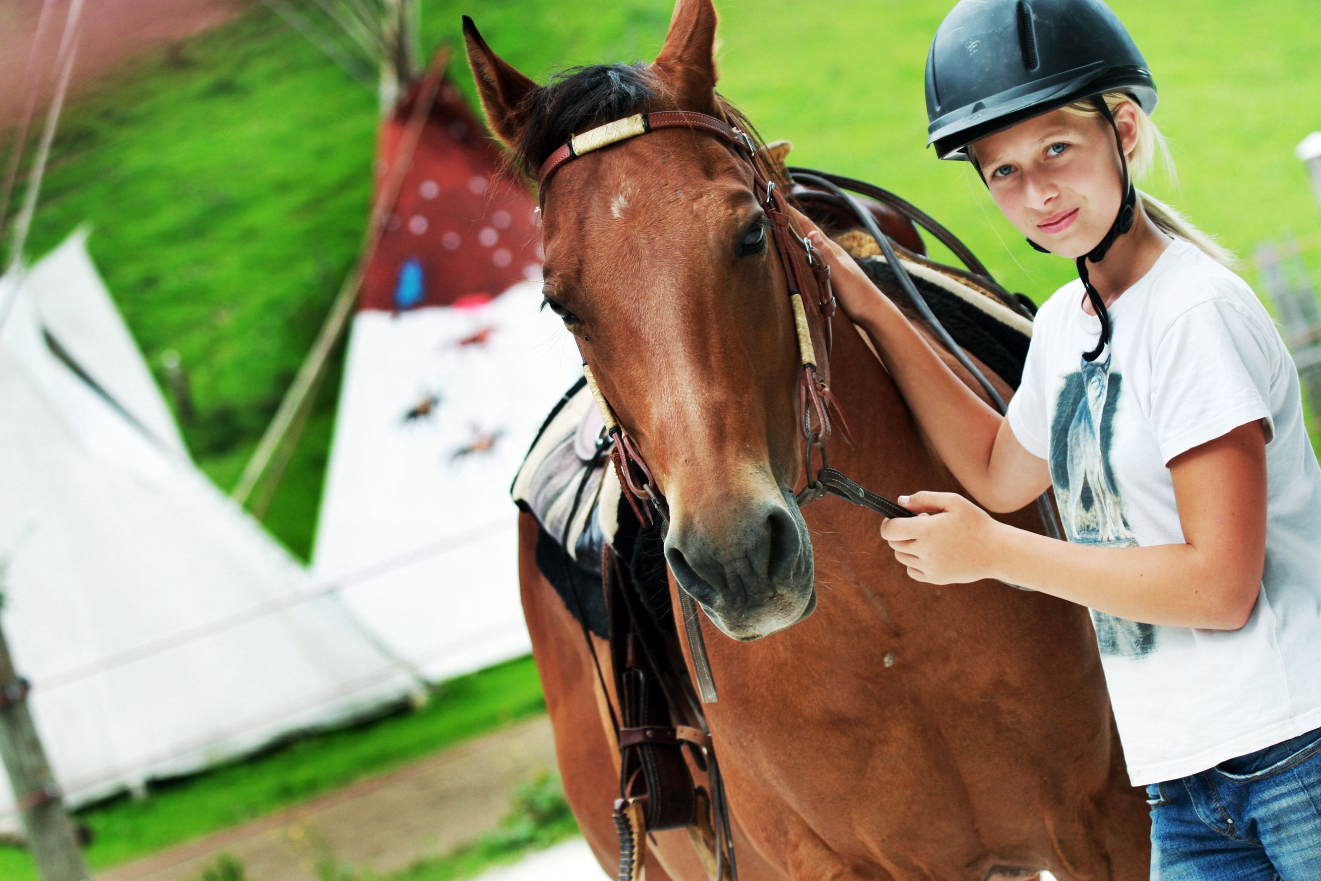 Ein Mädchen mit Helm steht neben einem braunen Pferd auf einem Bauernhof.