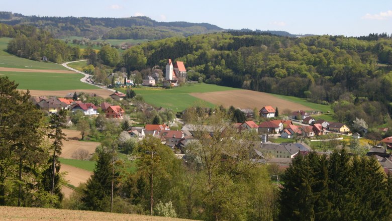 Landschaft mit Dorf, Kirche und Hügeln im Hintergrund.