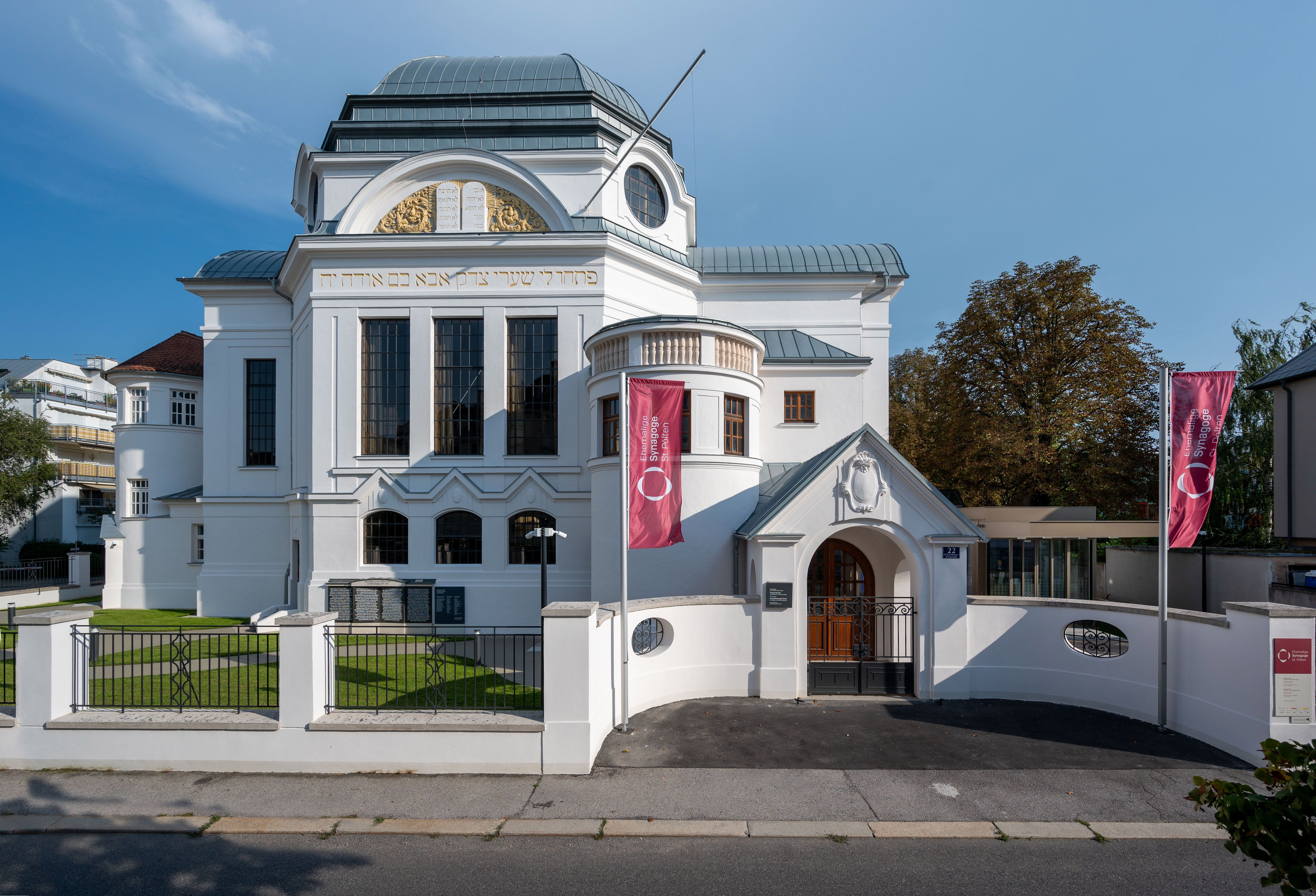 Ehemalige Synagoge in St. Pölten bei Dämmerung mit beleuchteten Fenstern und vorbeifahrendem Bus.