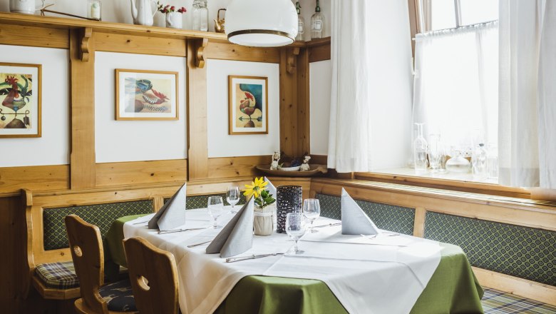 Gem&uuml;tliche Stube mit Holzm&ouml;beln, gedecktem Tisch und Bildern an der Wand.