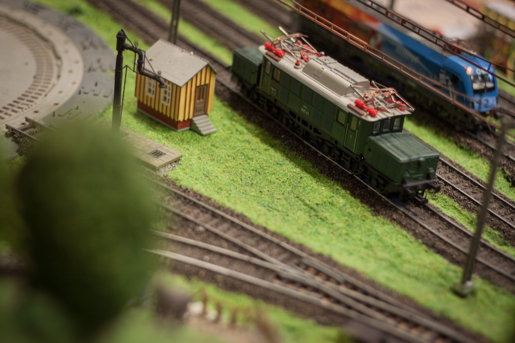 Modelleisenbahn mit grünem Zug und kleinem Gebäude auf einer Anlage.