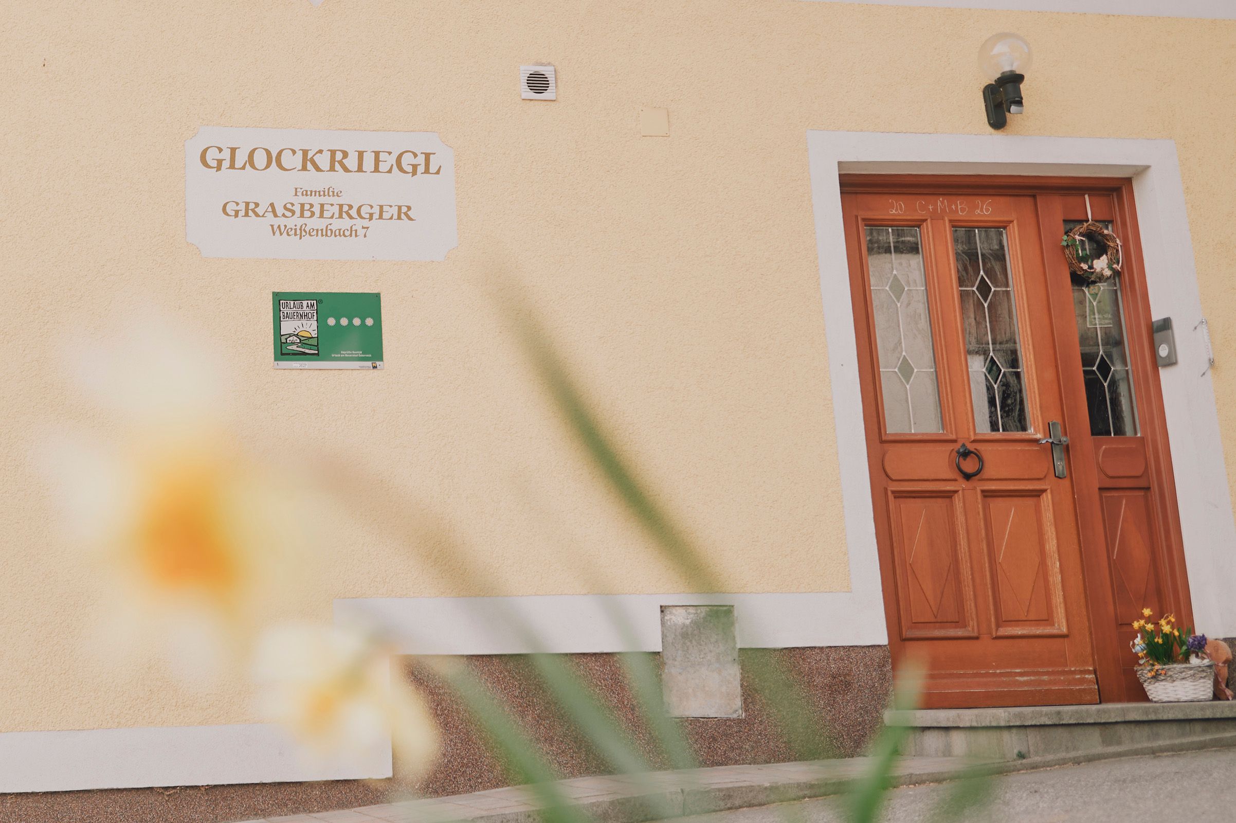 Eingangstür eines Gebäudes mit dem Schild 'Glockriegl' und einem Blumenkranz.