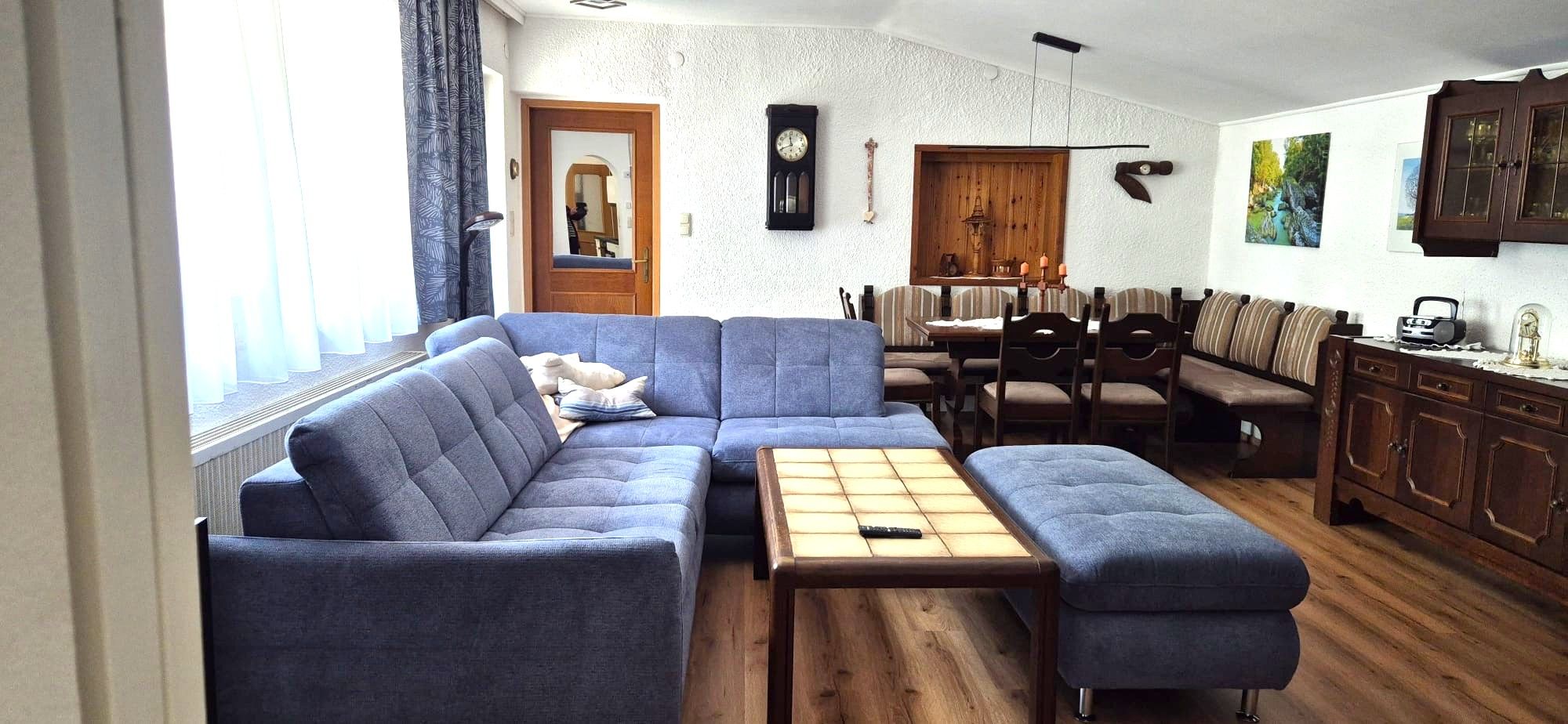 Gemütliches Wohnzimmer mit blauer Couch, Holztisch und Essbereich in einer Ferienwohnung.