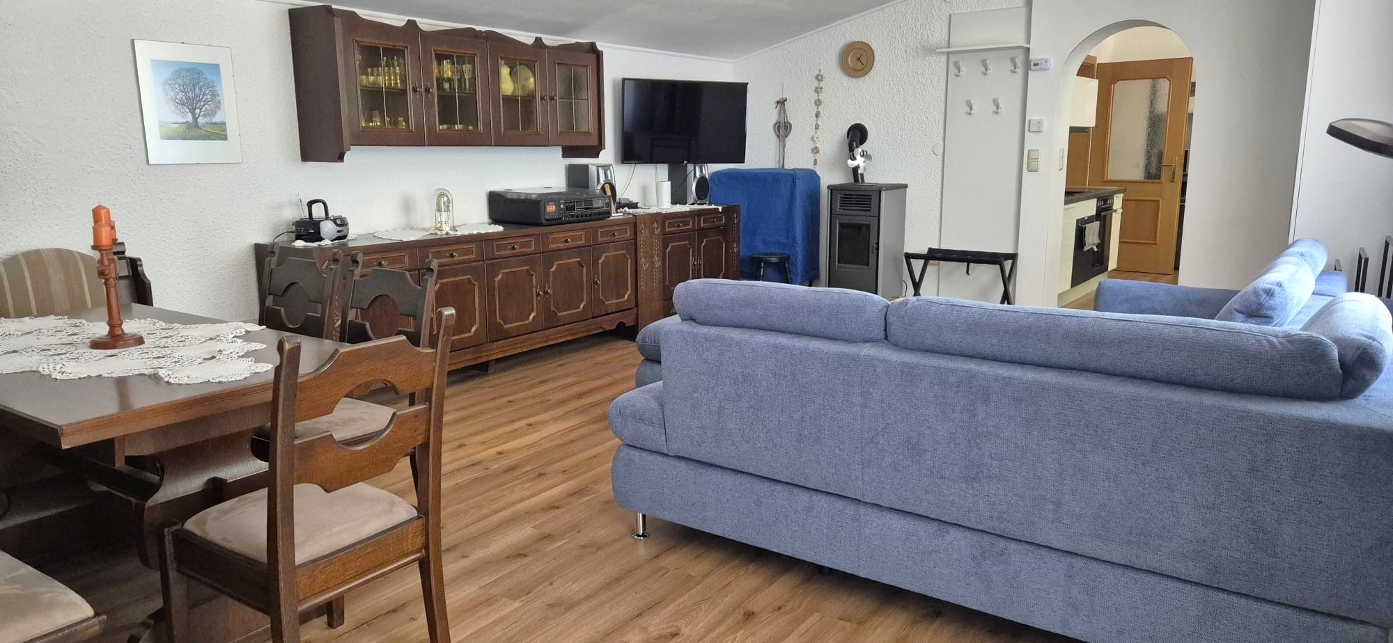 Wohnzimmer einer Ferienwohnung mit blauer Couch, Holzmöbeln und Esstisch.