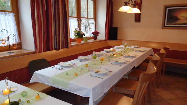 A festively laid table in an inn with white tablecloths, candles and flowers. Wooden furniture and windows with curtains in the background.