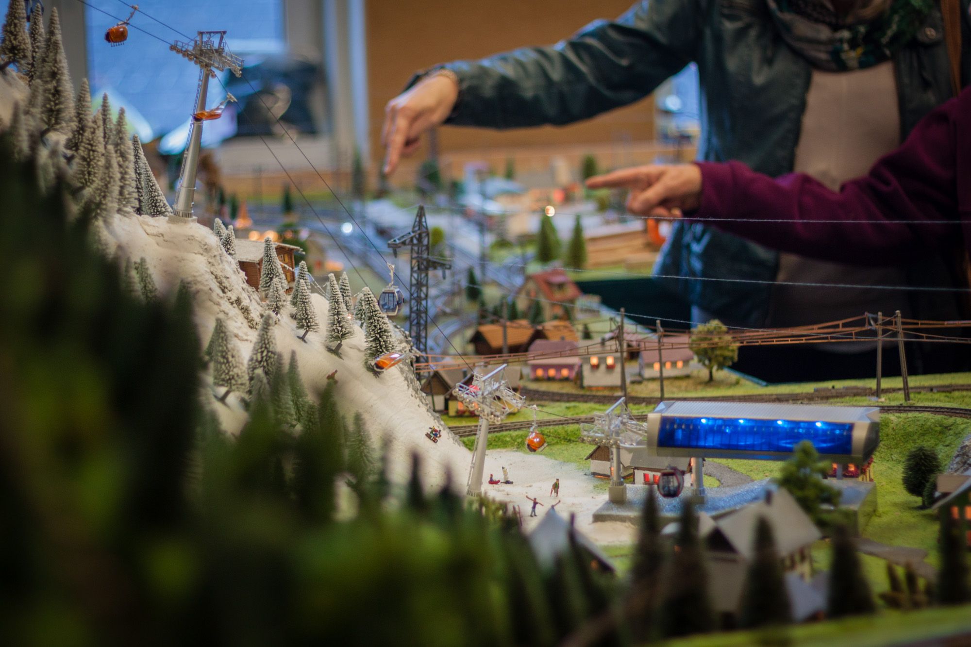 Detailreiche Modelllandschaft mit Seilbahn und schneebedeckten Bäumen, im Hintergrund zeigen zwei Personen auf das Modell.