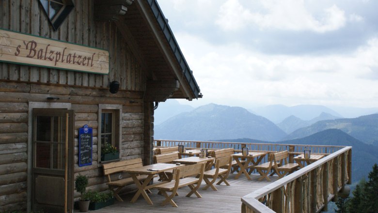 Wooden terrace with tables and benches in front of a mountain hut with a view of the Alps.