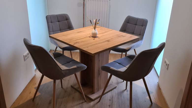 TDR-GasthofKirchenwirth-Esstisch, © Josef Burger Ein moderner Esstisch mit vier grauen Stühlen in einem hellen Raum.