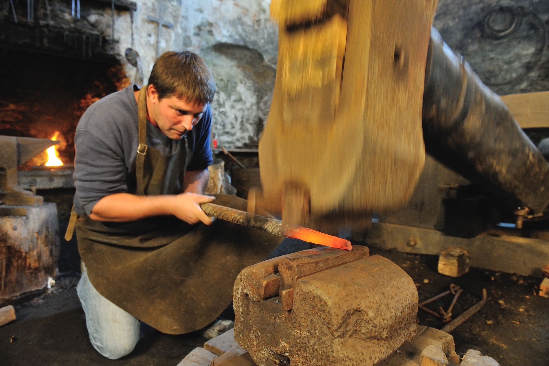 Ein Schmied bearbeitet glühendes Metall mit einem Hammer in einer Werkstatt.