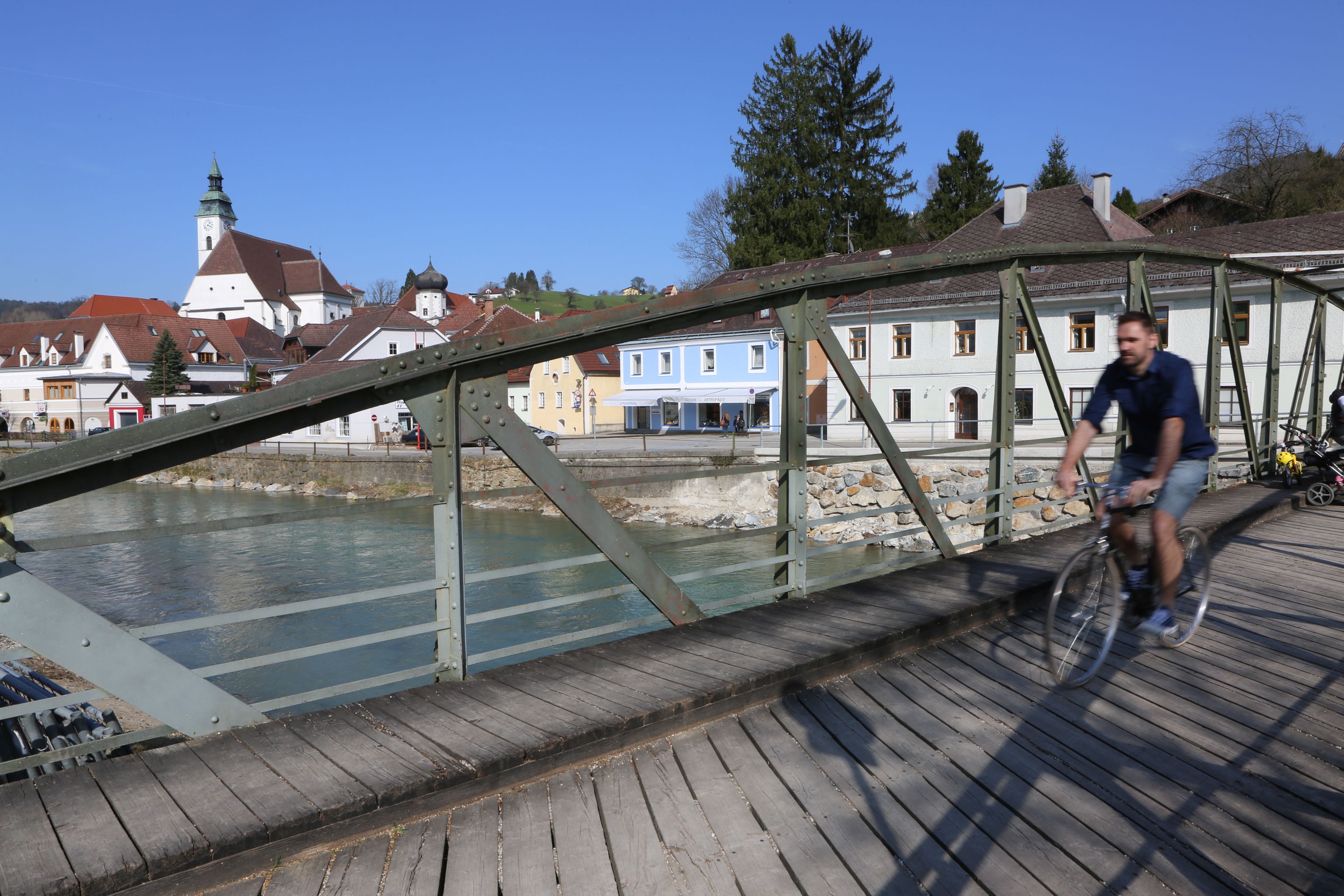 Ein Radfahrer überquert die Töpperbrücke in einer malerischen Stadt mit Kirche und bunten Häusern im Hintergrund.