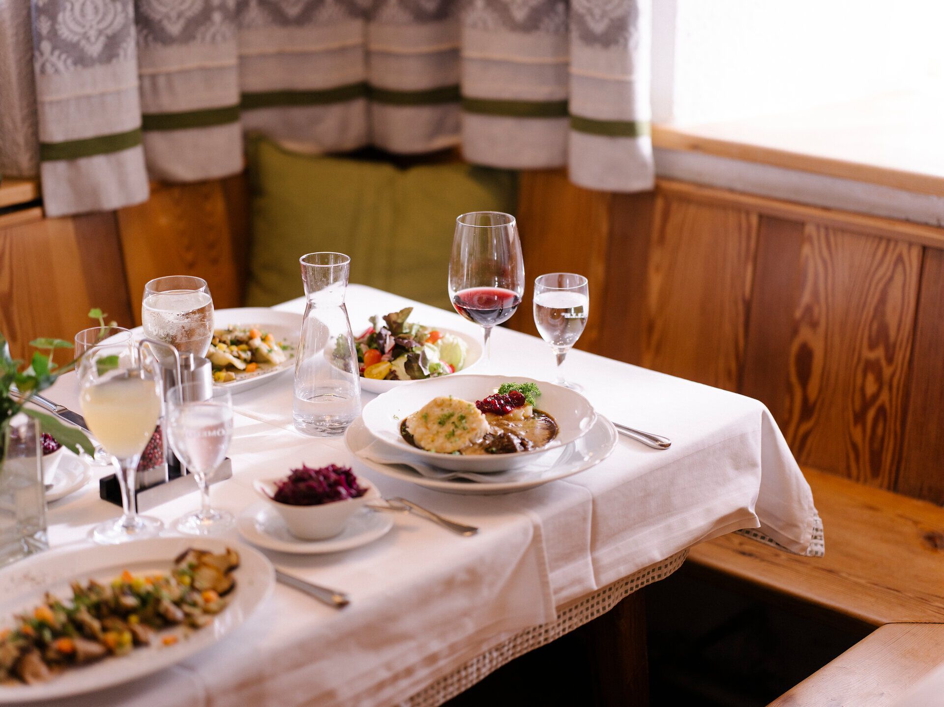 In einem einladenden Gasthof, umgeben von rustikalem Holz und gemütlicher Atmosphäre, genießen Gäste ein festliches Mahl. Die Tische sind liebevoll gedeckt, während köstliche Speisen und erlesene Weine auf die Besucher warten. Hier wird die Wirtshauskultur Niederösterreichs in vollen Zügen zelebriert.