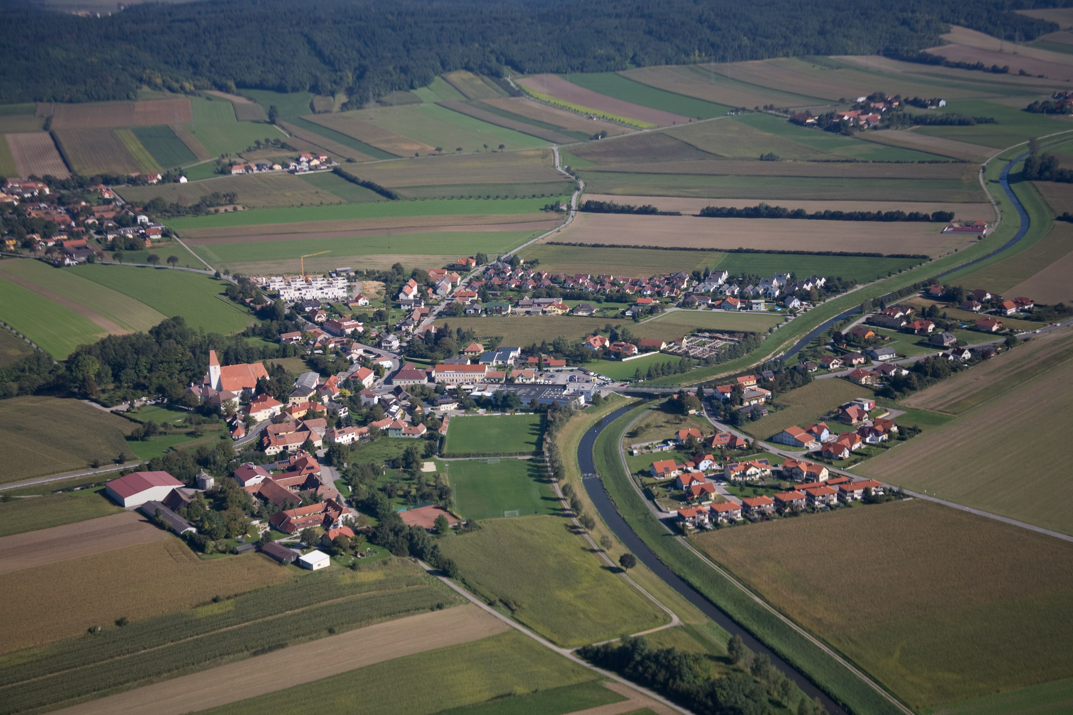 Luftaufnahme eines Dorfes mit umliegenden Feldern und einem Fluss.