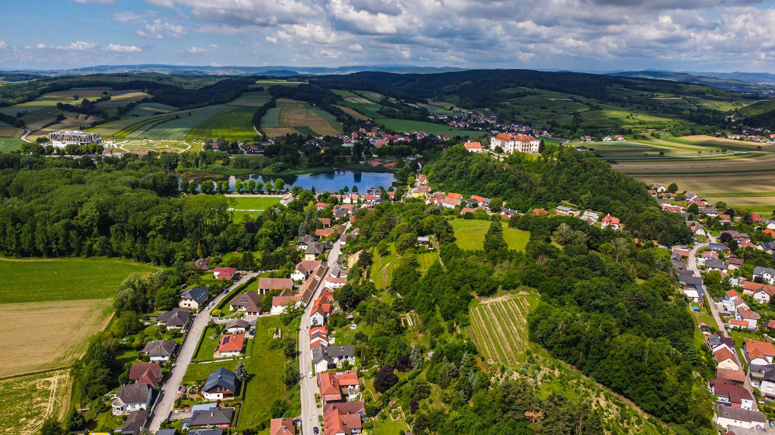 Luftaufnahme einer ländlichen Region mit Feldern, einem See und einem Schloss auf einem Hügel.