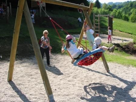 Kinder schaukeln auf einem Spielplatz in einer Nestschaukel.