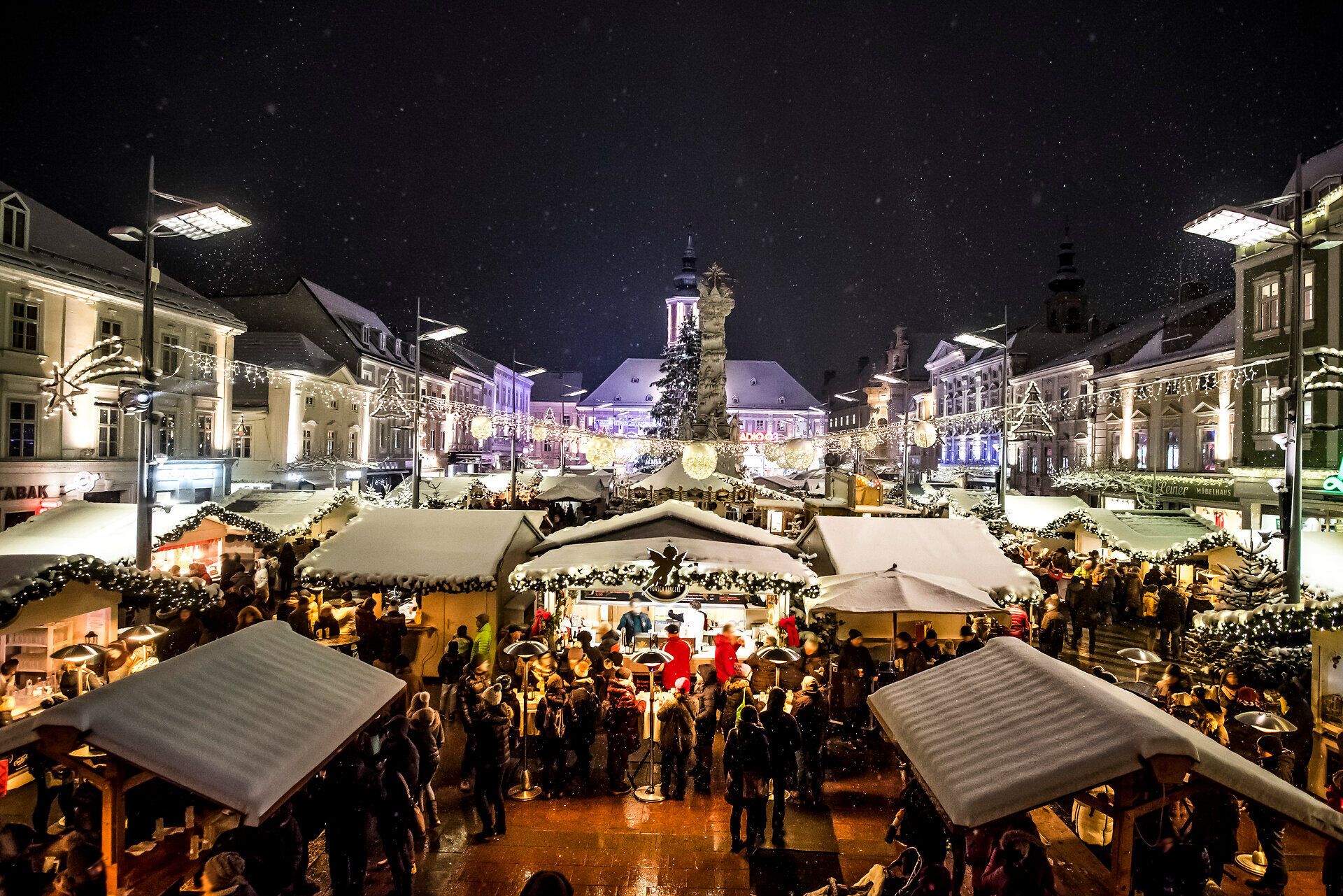Der Adventmarkt erstrahlt in festlichem Glanz, während sanfter Schnee die Stände bedeckt. Besucher schlendern zwischen liebevoll dekorierten Hütten, die köstliche Leckereien und handgefertigte Geschenke anbieten. Die warme Atmosphäre und der Duft von Glühwein laden zum Verweilen ein.