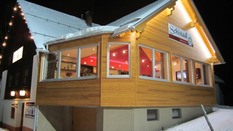 Ein beleuchtetes Gebäude im Schnee mit dem Schild 'Schistadl'.