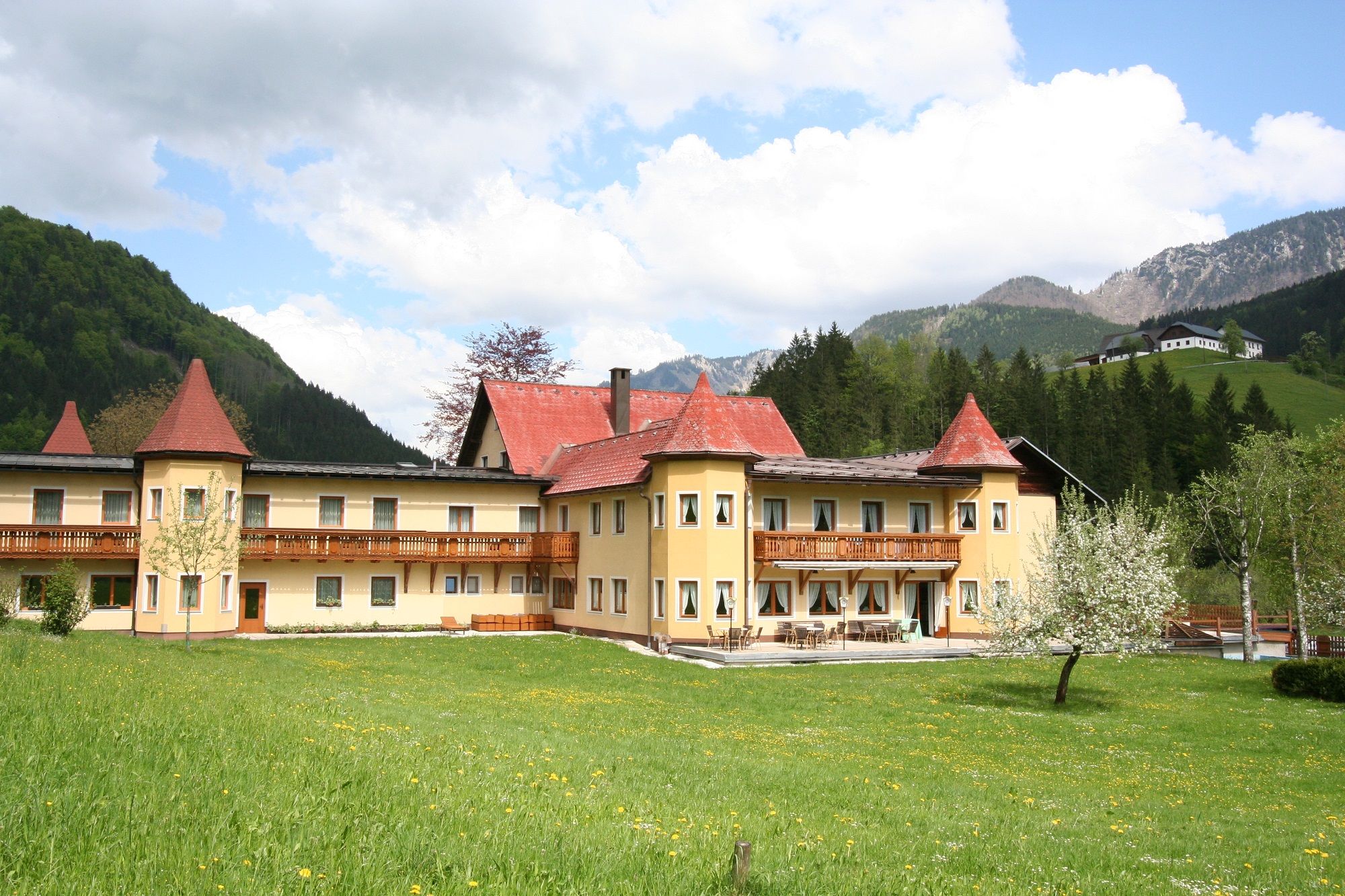 Ein großes Hotel mit roten Dächern in einer grünen, bergigen Landschaft.