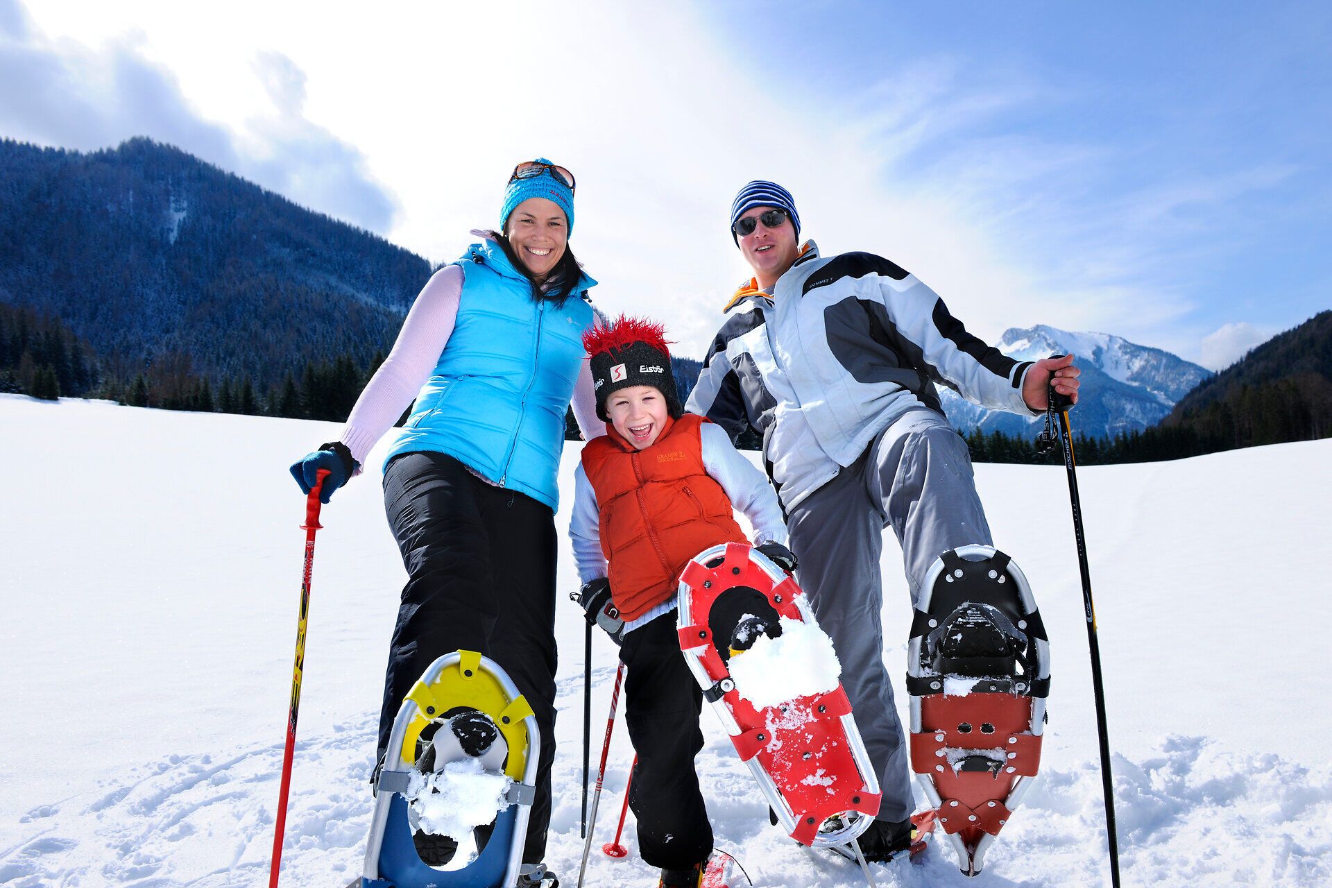 In der winterlichen Landschaft des Naturparks Eisenwurzen genießen eine Familie und ihr Kind die Freude am Schneeschuhwandern. Umgeben von schneebedeckten Bergen und strahlend blauem Himmel strahlt die Szene eine herzliche und abenteuerliche Atmosphäre aus.