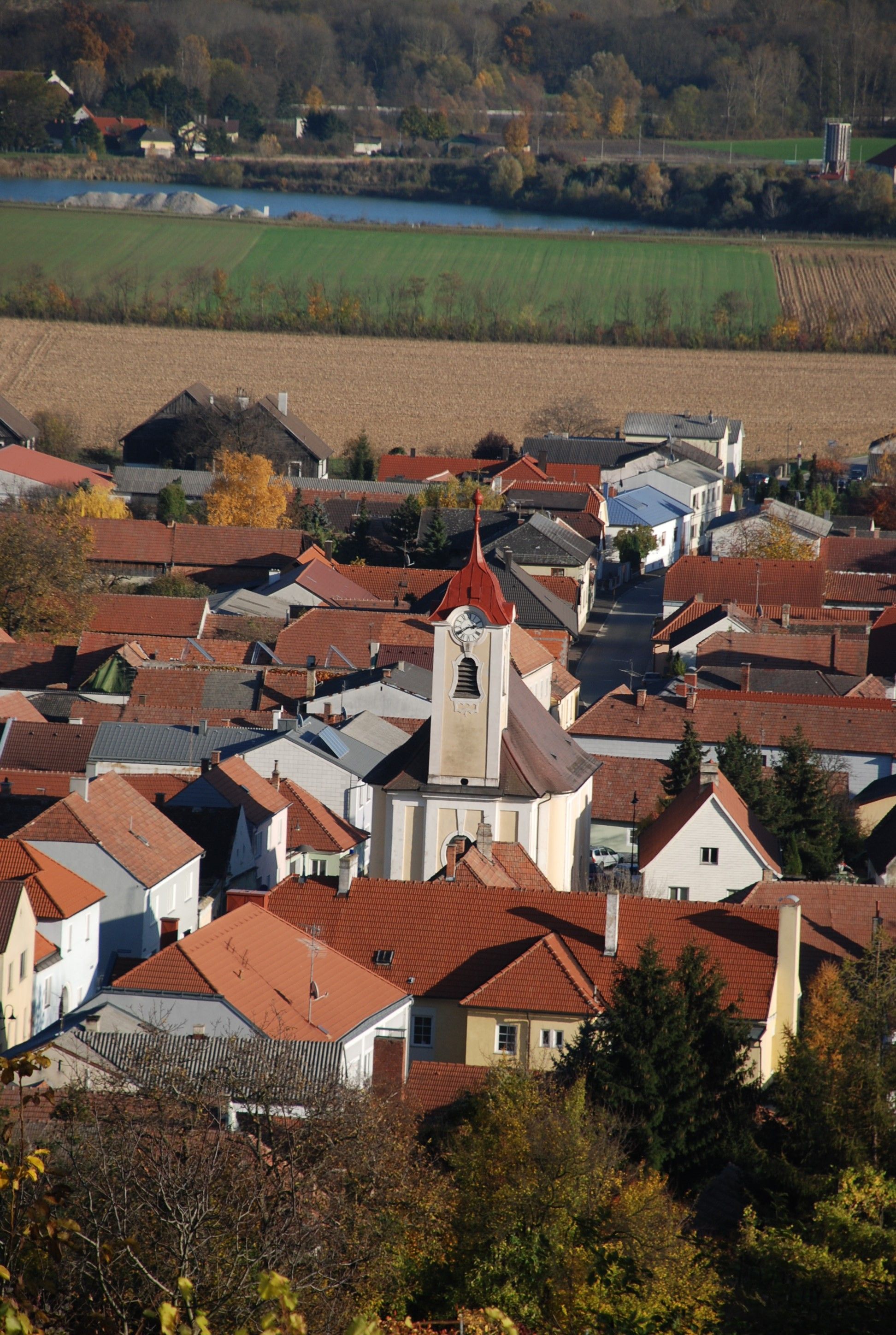Luftaufnahme der Pfarrkirche Getzersdorf mit umliegenden Häusern und Feldern im Herbst.