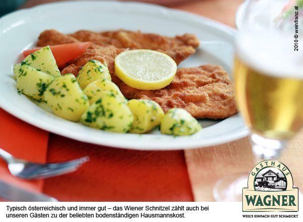 Ein Teller mit Wiener Schnitzel, Petersilienkartoffeln und einer Zitronenscheibe, daneben ein Glas Bier.