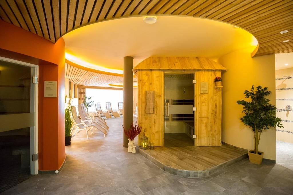 Innenansicht einer Saunalandschaft mit Holzsauna und Liegestühlen.