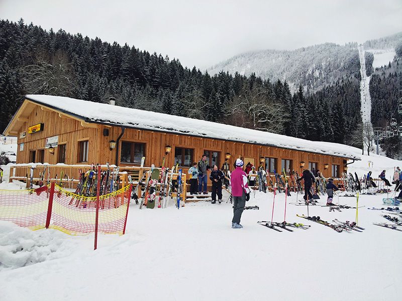 Skihütte im Schnee mit Skifahrern und Ausrüstung davor.