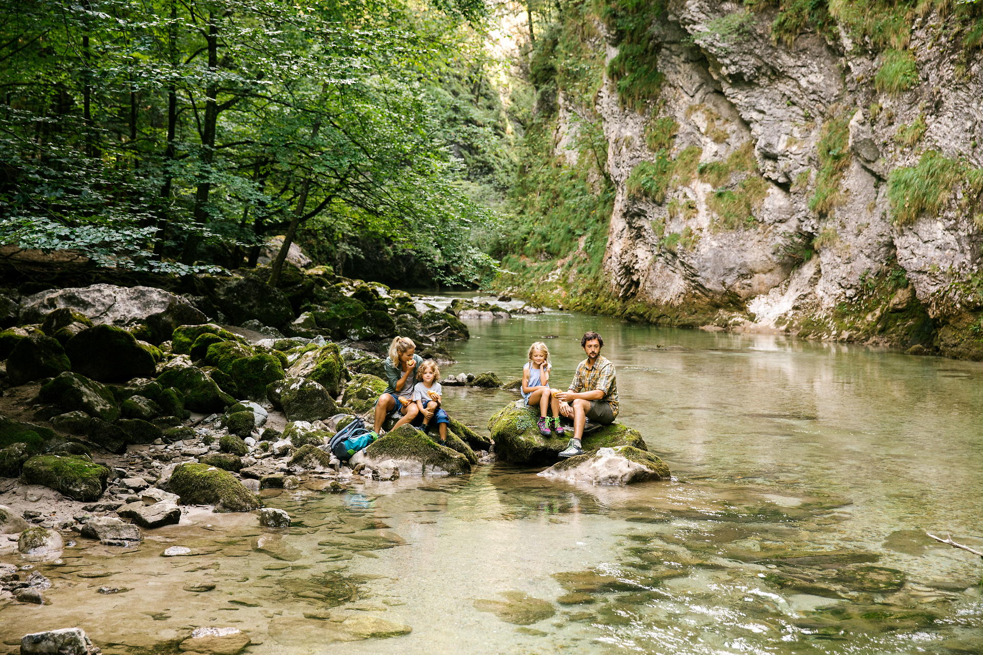 Ein erfrischender Moment in der Natur, wo eine Familie am Ufer eines glasklaren Baches sitzt. Umgeben von üppigem Grün und sanften Felsen, genießen sie die Ruhe und die Schönheit des Naturparks Ötscher Tormäuer.