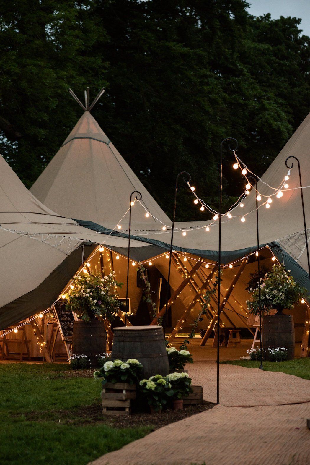 Ein beleuchtetes Tipi-Zelt für eine Veranstaltung, umgeben von Pflanzen und Lichterketten.