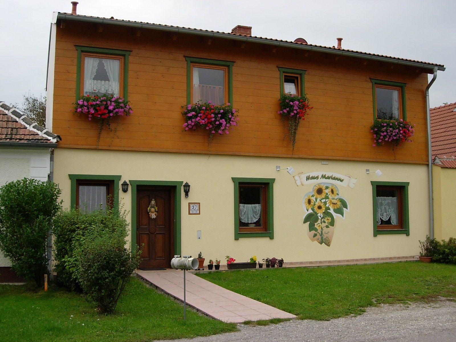 Zweistöckiges Haus mit Holzverkleidung und Blumenkästen, beschriftet als 'Haus Marianne'.