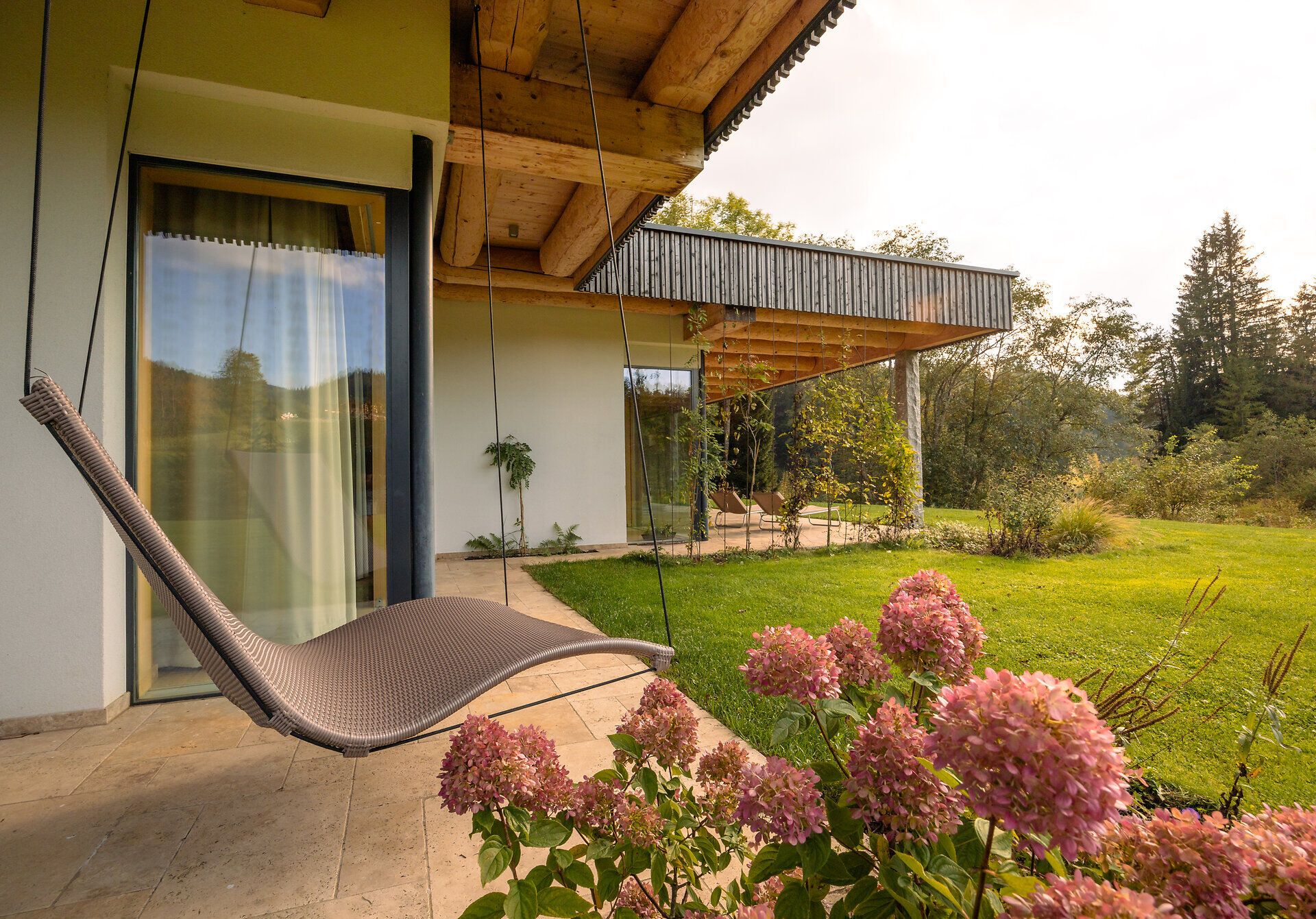 Ein einladendes Ferienhaus am See, umgeben von üppigem Grün und blühenden Hortensien. Die sanfte Schwinge der Hängematte lädt dazu ein, die Ruhe der Natur zu genießen und den Blick über die malerische Landschaft schweifen zu lassen.