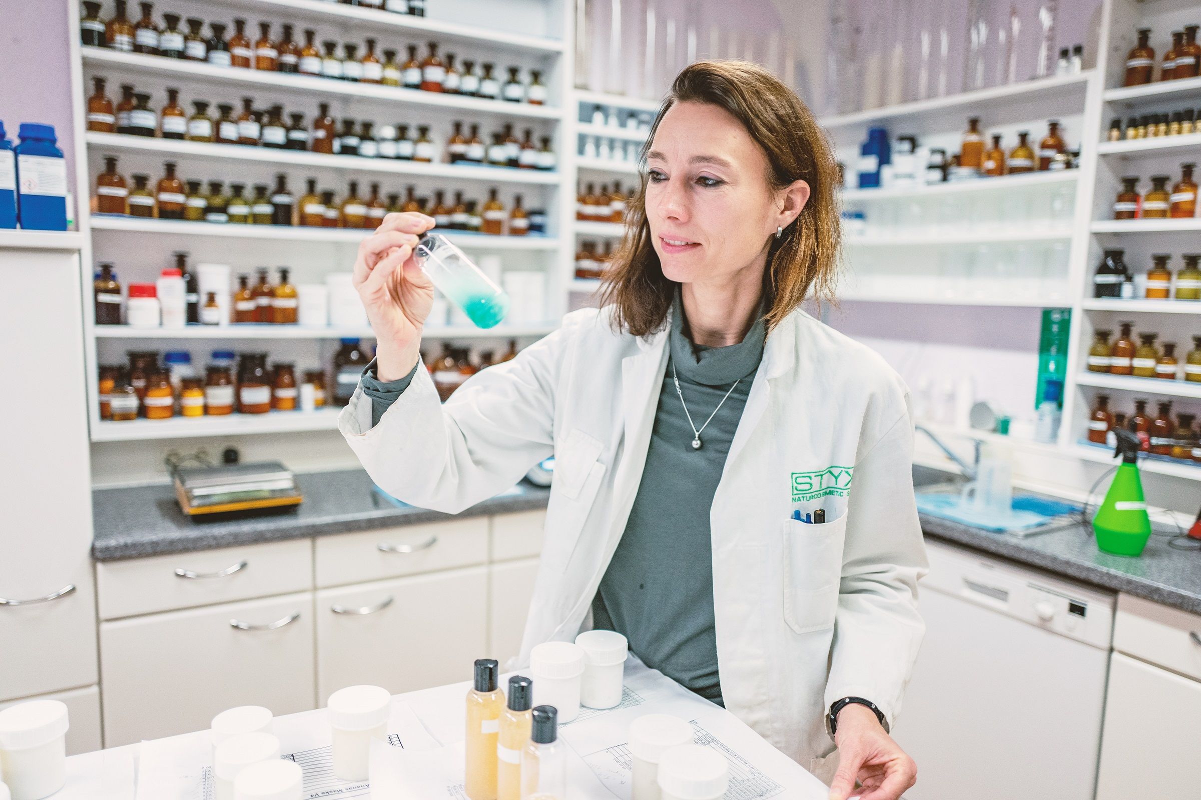 Eine Frau im weißen Laborkittel hält ein Reagenzglas mit blauer Flüssigkeit in einem Labor.