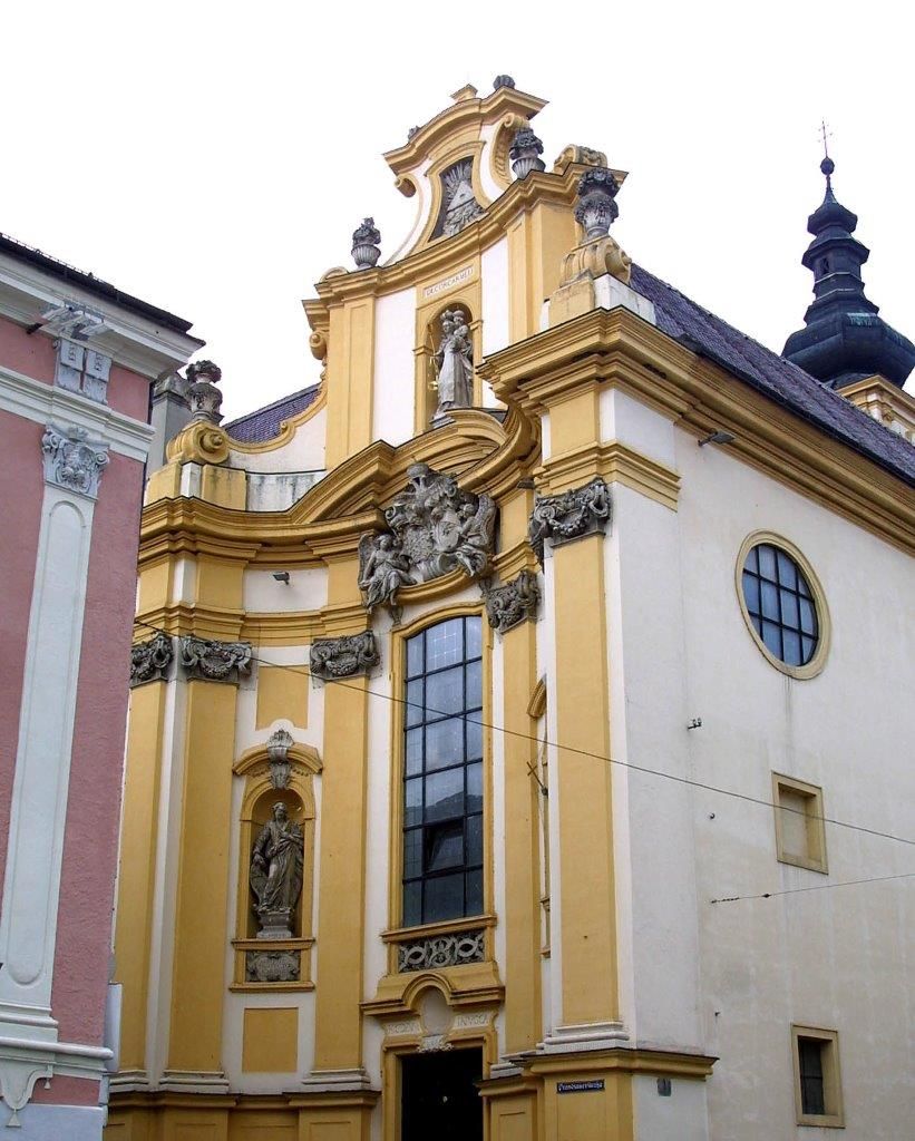 Barocke Kirche mit gelber Fassade und Statuen.