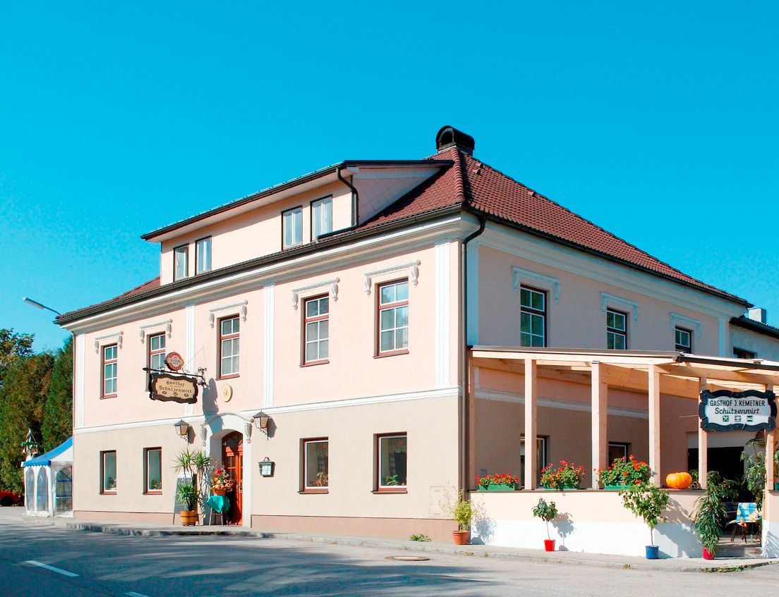 Ein traditionelles Gasthaus mit rosa Fassade und rotem Dach, dekoriert mit Pflanzen und einem Kürbis.