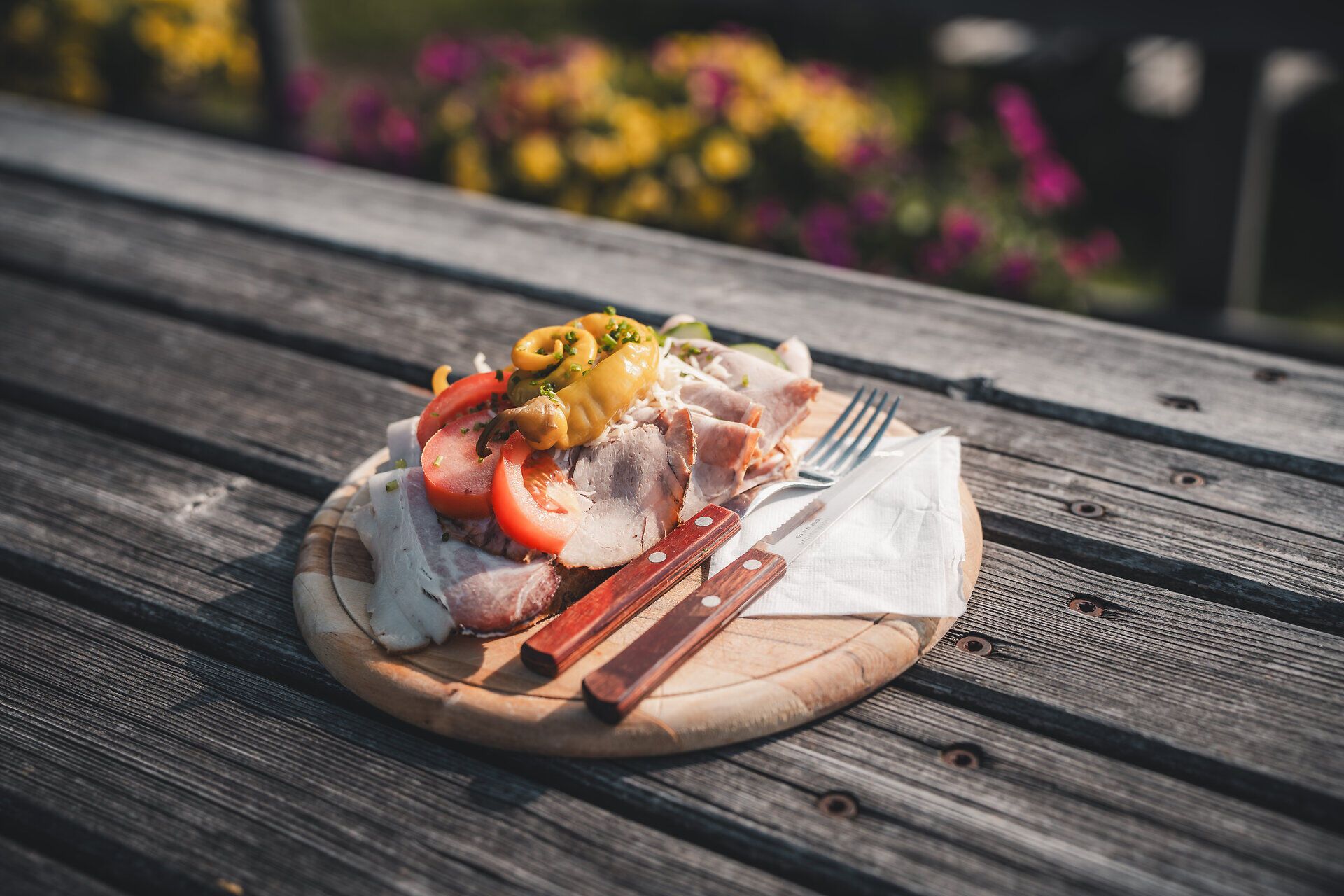 Eine deftige Jause auf einem Holztisch: Brot, Käse, Speck und Aufstriche auf rot-weißem Tischtuch – regionale Mostviertler Spezialitäten.
