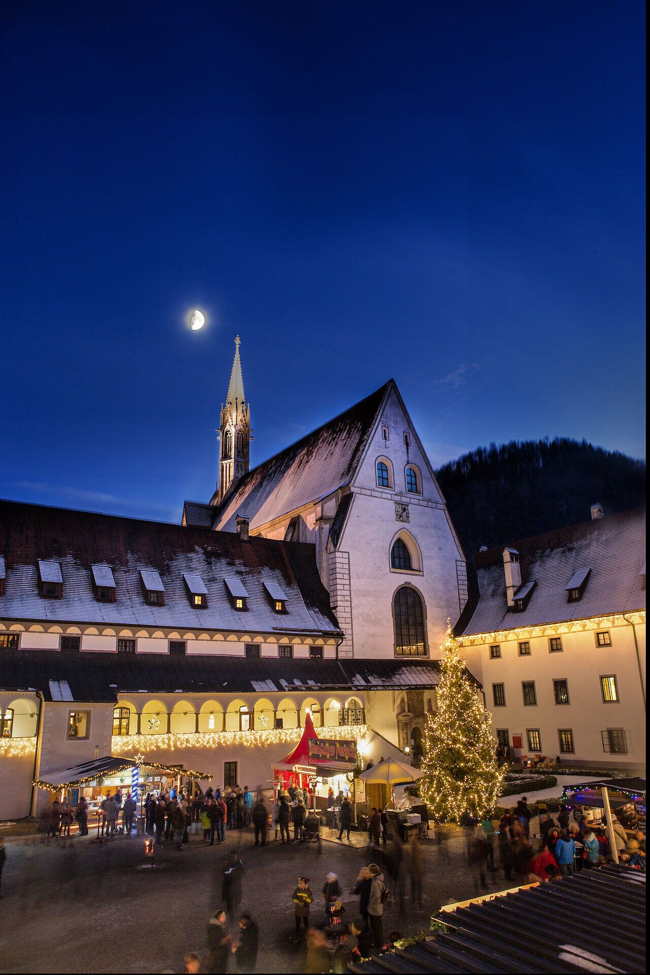 In der festlich erleuchteten Kulisse des Adventmarktes entfaltet sich eine zauberhafte Atmosphäre. Der Duft von Glühwein und frisch gebrannten Mandeln zieht durch die Luft, während die sanften Lichter der Weihnachtsdekoration die Herzen der Besucher erwärmen. Ein majestätischer Weihnachtsbaum steht stolz im Zentrum und lädt zum Verweilen und Genießen ein.