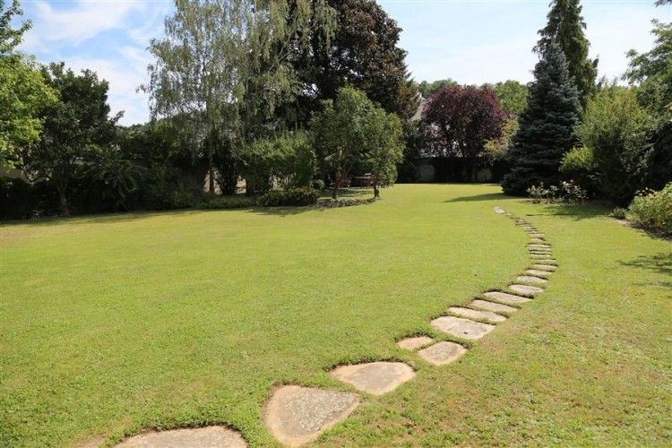 Ein gepflegter Garten mit einem geschwungenen Steinweg und Bäumen im Hintergrund.