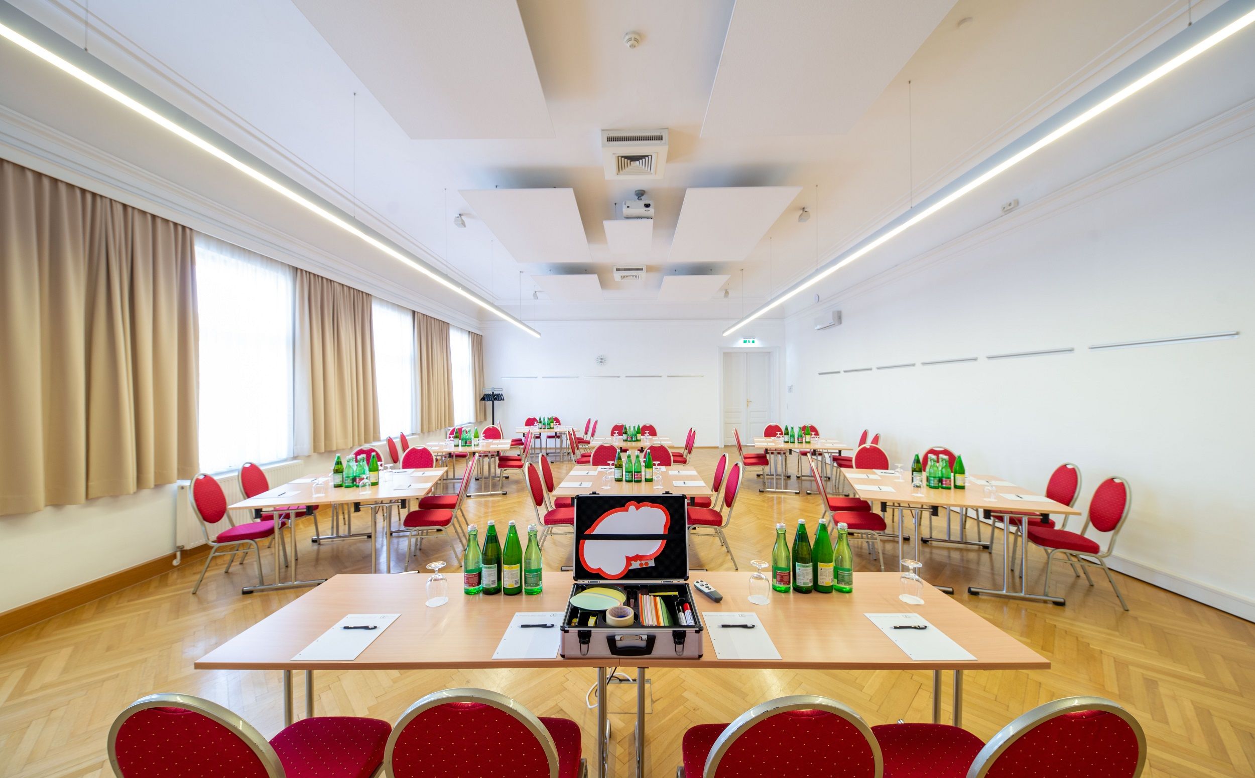 Ein heller Seminarraum mit roten Stühlen und Tischen, auf denen Wasserflaschen und Schreibmaterialien stehen.