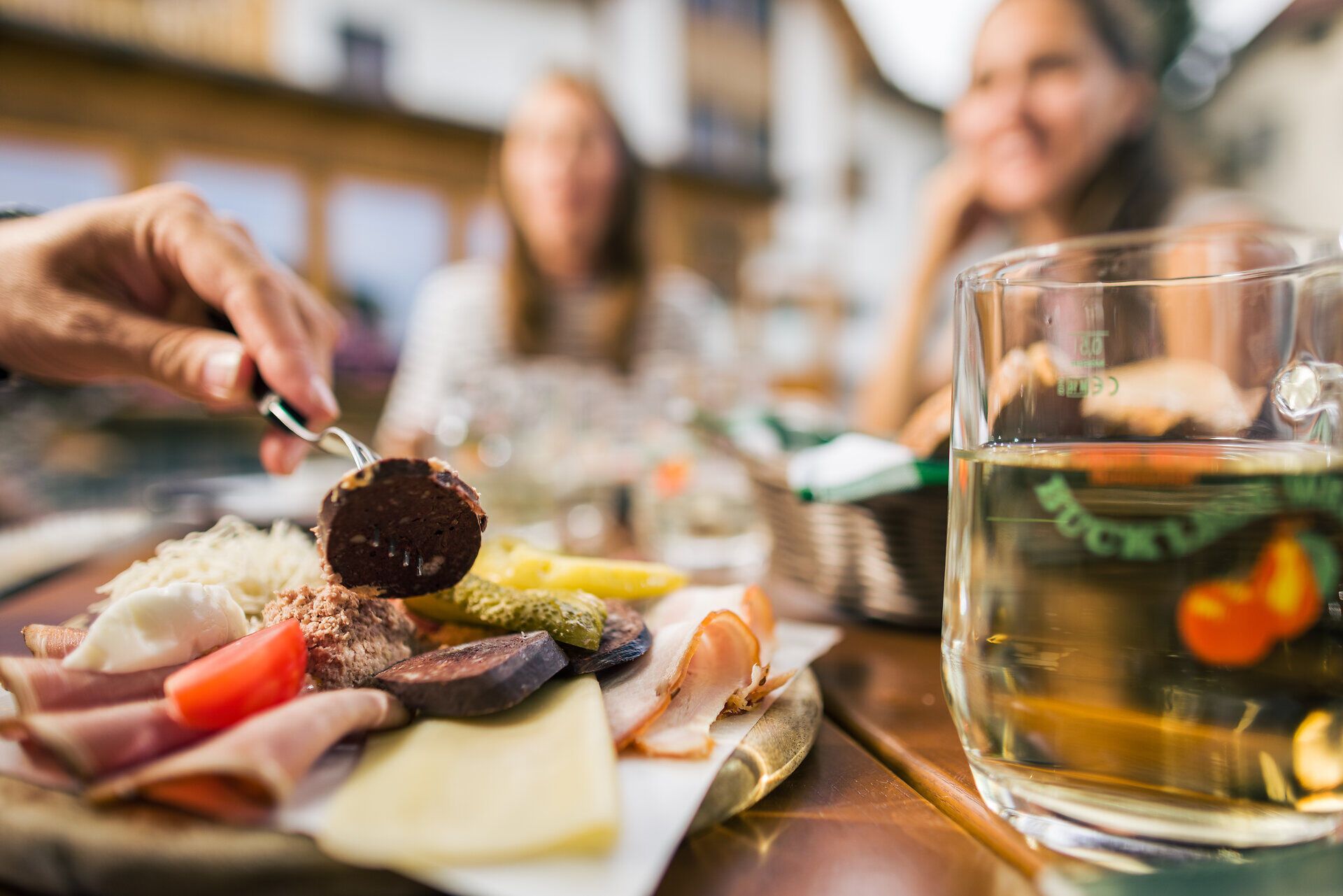 Am Tisch steht eine appetitlich garnierte Heurigenjause mit ausgewählten Köstlichkeiten und ein gefülltes Glas. 