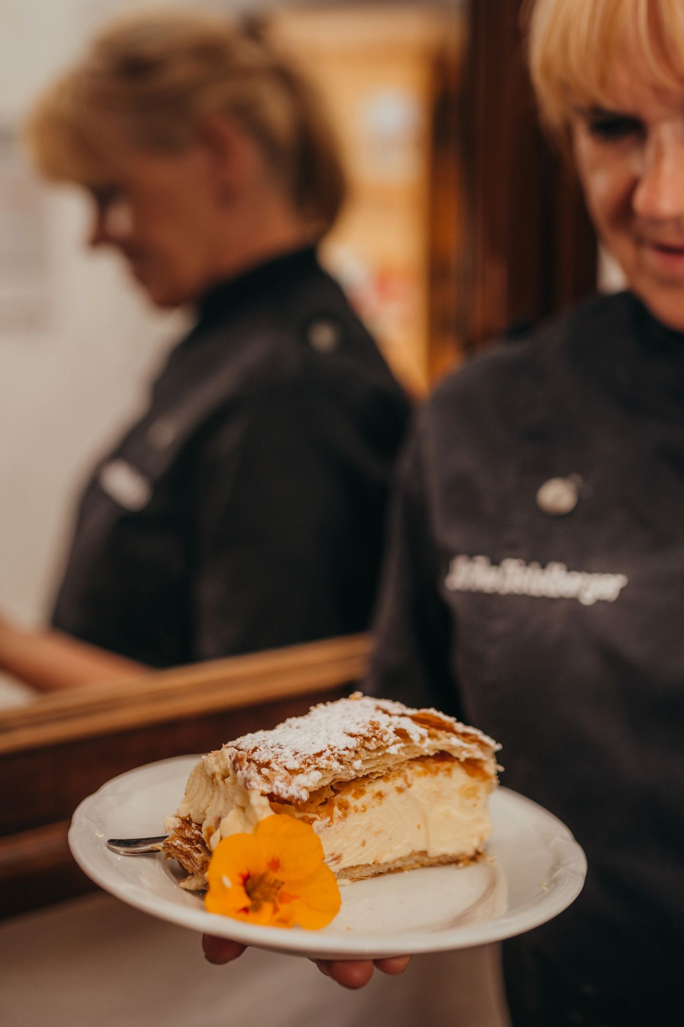 Eine Person hält einen Teller mit einem Stück Torte, dekoriert mit einer Blume.