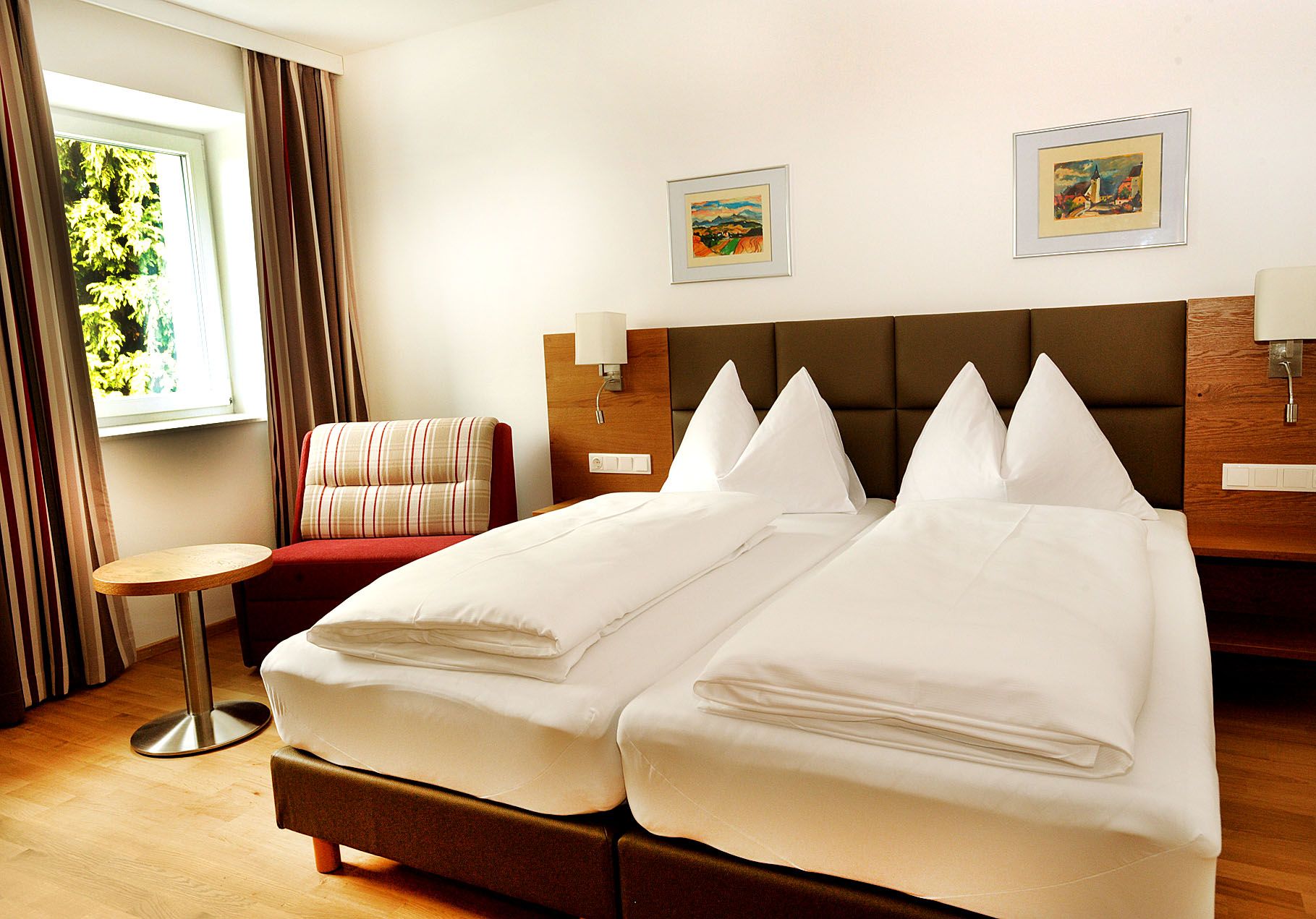 Ein modernes Hotelzimmer mit Doppelbett, Sessel, kleinem Tisch und zwei Bildern an der Wand.