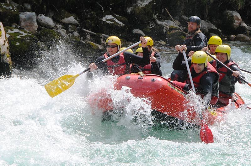 Gruppe beim Rafting auf einem Fluss mit gelben Helmen und roten Westen.