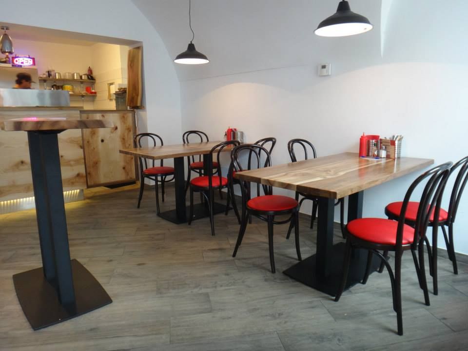 Innenansicht eines modernen Restaurants mit Holztischen und roten Stühlen.