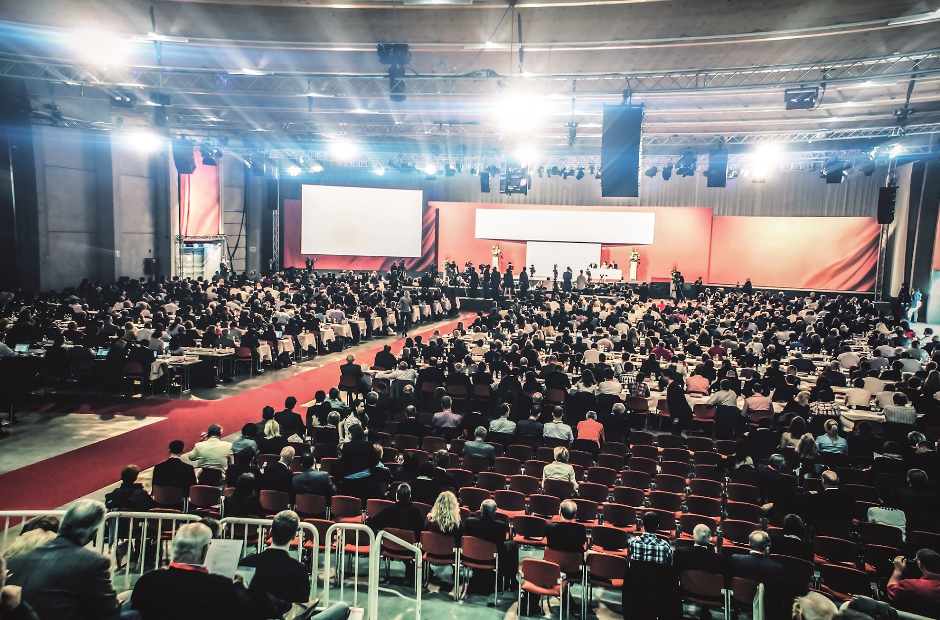 Großer Kongresssaal mit vielen Teilnehmern, Bühne und Leinwand.
