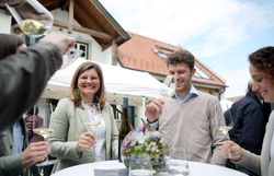 Inmitten einer festlichen Atmosphäre genießen die Gäste erlesene Weine und kulinarische Köstlichkeiten. Die fröhlichen Gesichter und das Anstoßen mit Gläsern schaffen eine einladende Stimmung, die zum Verweilen einlädt.
