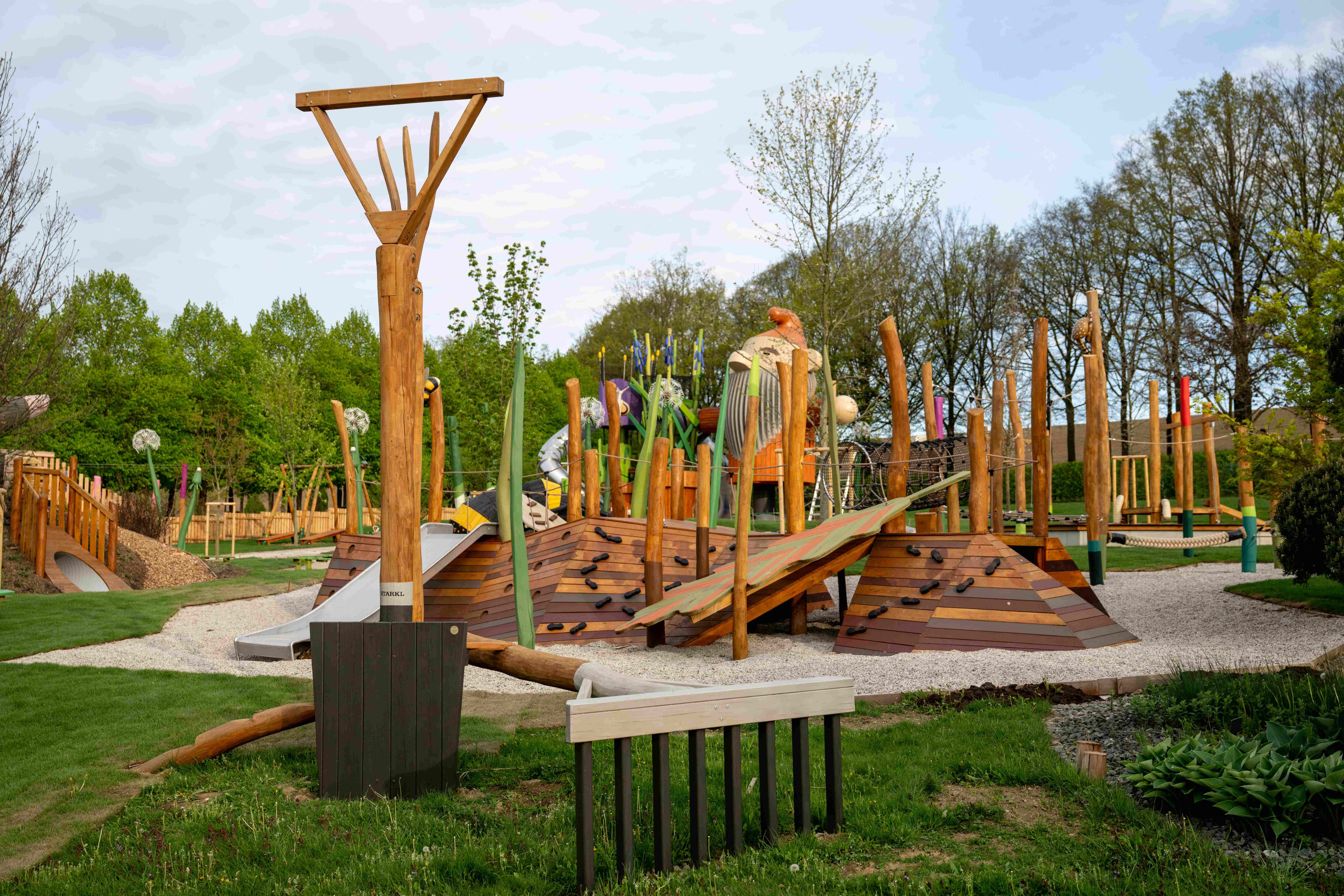 Ein moderner Spielplatz mit Holzstrukturen und Kletterelementen in einem grünen Park.
