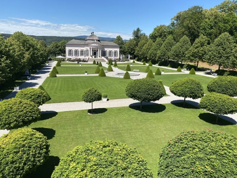 Barocker Park mit symmetrischen Wegen, gepflegten Rasenflächen und einem Pavillon im Hintergrund.