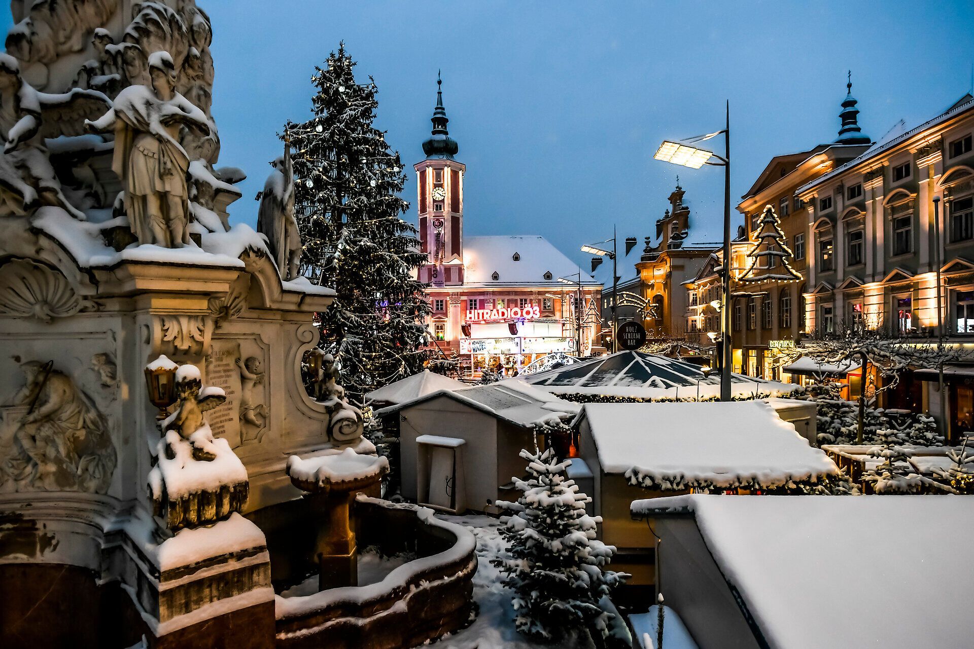 Der Adventmarkt erstrahlt in festlichem Glanz, während sanfte Schneeflocken die Umgebung in eine zauberhafte Winterlandschaft verwandeln. Die warmen Lichter der Stände laden dazu ein, die köstlichen Spezialitäten der Region zu probieren und die besinnliche Atmosphäre zu genießen.